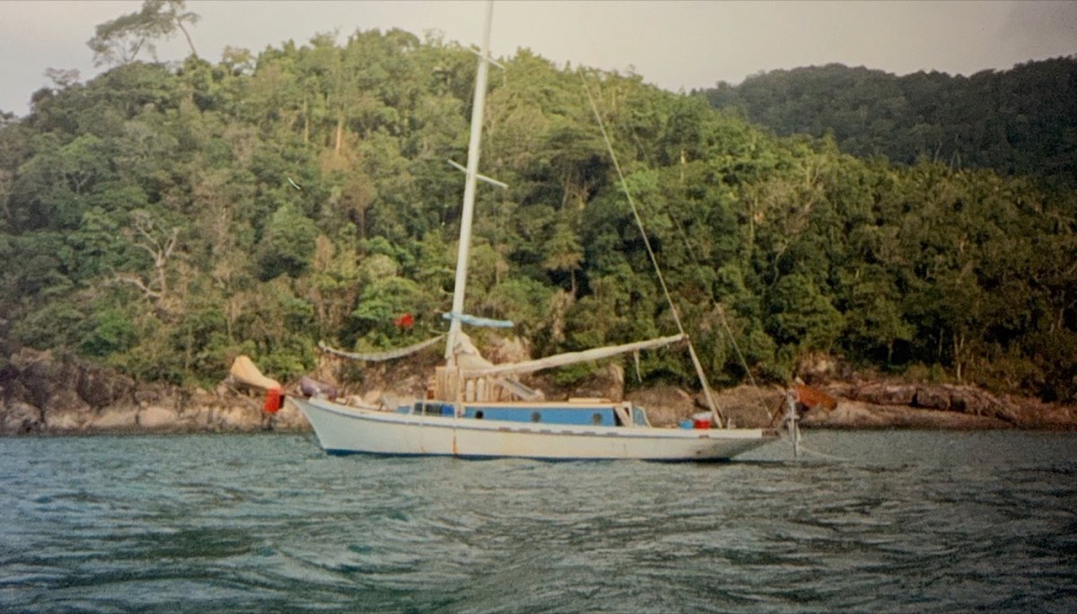 A sailboat at anchor under jungle hills